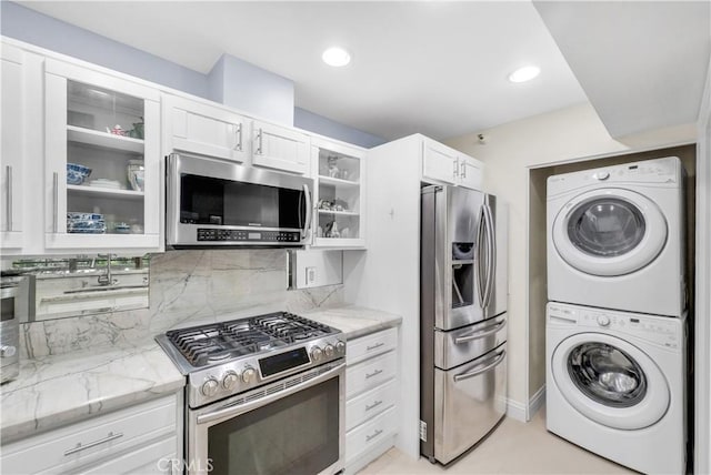 kitchen featuring white cabinetry, stacked washer and clothes dryer, stainless steel appliances, tasteful backsplash, and light stone countertops