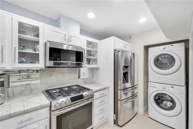 260 Cagney Ln Unit 105, Newport Beach, CA 92663 - kitchen featuring stainless steel appliances, stacked washer / drying machine, light stone countertops, glass insert cabinets, and white cabinets