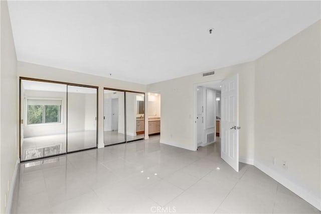 unfurnished bedroom featuring ensuite bath, light tile patterned floors, and multiple closets