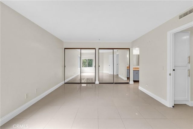 unfurnished bedroom featuring light tile patterned flooring, connected bathroom, and multiple closets