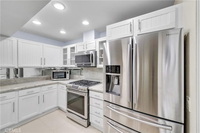 260 Cagney Ln Unit 105, Newport Beach, CA 92663 - kitchen featuring appliances with stainless steel finishes, white cabinets, glass insert cabinets, light stone counters, and light tile patterned floors