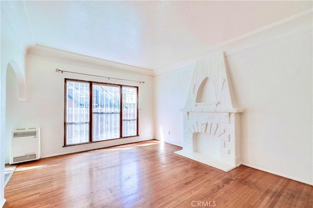 unfurnished living room featuring a large fireplace, heating unit, hardwood / wood-style floors, and ornamental molding