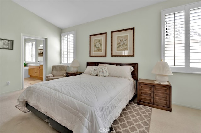 bedroom with light colored carpet, lofted ceiling, and ensuite bathroom