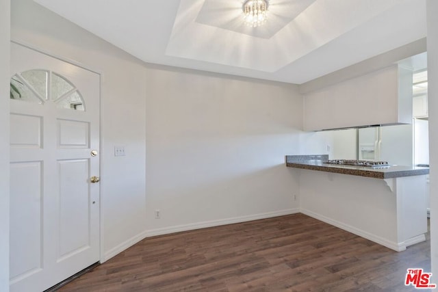 kitchen featuring kitchen peninsula, dark hardwood / wood-style flooring, a tray ceiling, stainless steel gas cooktop, and white refrigerator with ice dispenser