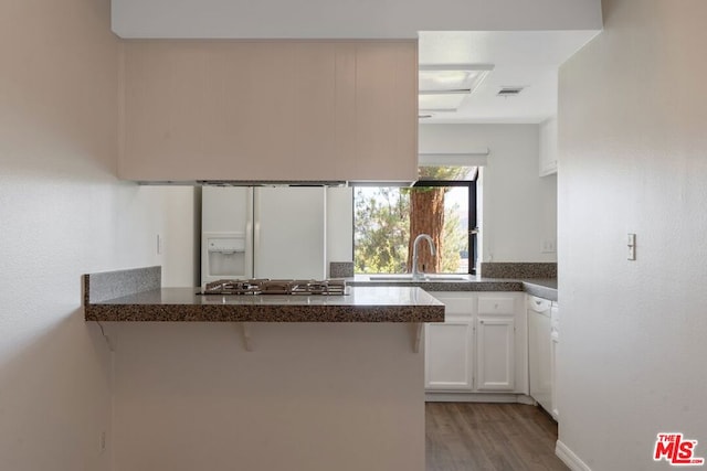 kitchen with kitchen peninsula, sink, white refrigerator with ice dispenser, white cabinetry, and a breakfast bar area