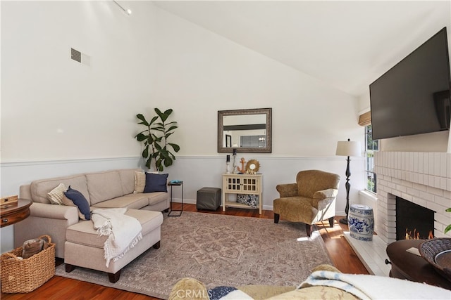 living room featuring high vaulted ceiling, a brick fireplace, and hardwood / wood-style flooring