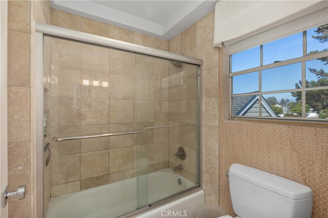 bathroom featuring shower / bath combination with glass door, tile walls, and toilet