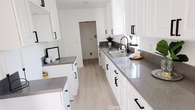 kitchen with white cabinets, light wood-type flooring, sink, and dark stone counters