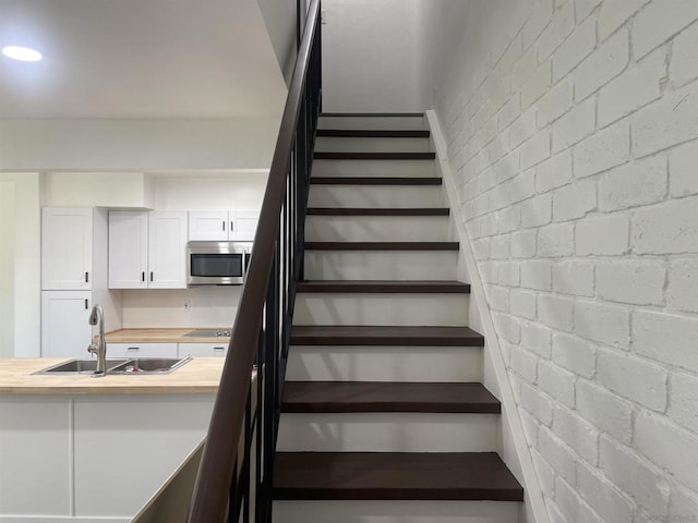 staircase featuring sink and brick wall