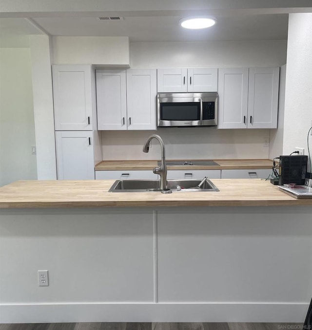 kitchen featuring kitchen peninsula, hardwood / wood-style flooring, white cabinetry, and sink