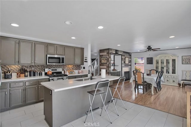 kitchen with stainless steel appliances, a sink, ceiling fan, light countertops, and backsplash