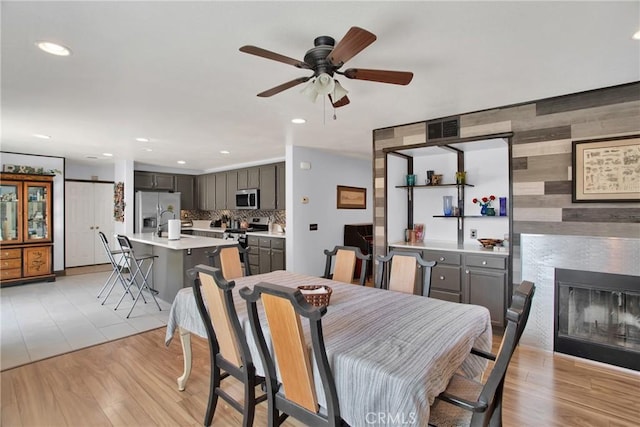 dining room featuring ceiling fan, recessed lighting, a glass covered fireplace, an accent wall, and light wood-style floors