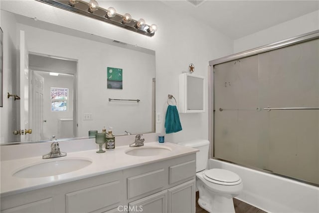 bathroom featuring toilet, double vanity, and bath / shower combo with glass door