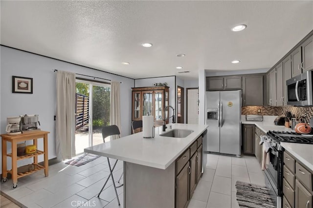 kitchen featuring stainless steel appliances, a sink, light countertops, tasteful backsplash, and a center island with sink