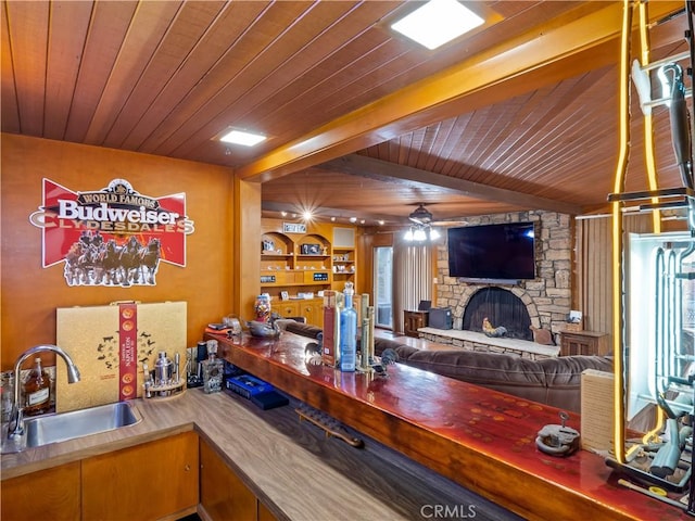 bar featuring a stone fireplace, ceiling fan, sink, and wooden ceiling