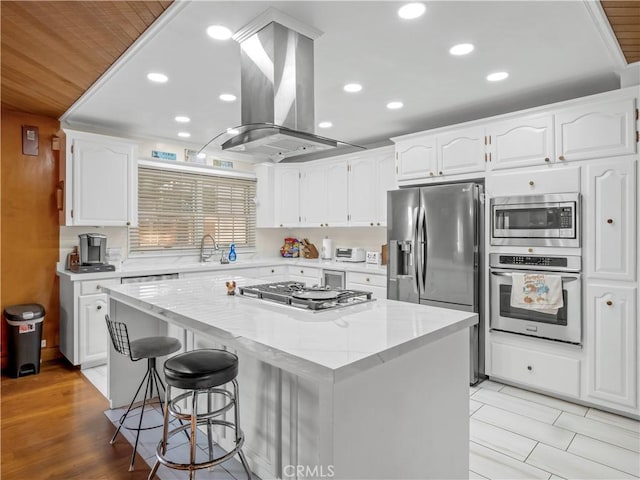 kitchen with a center island, sink, island range hood, white cabinets, and appliances with stainless steel finishes