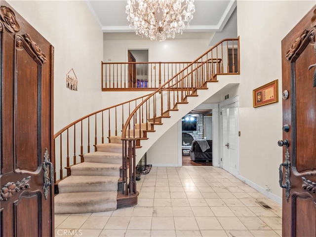 entryway with a notable chandelier, light tile patterned floors, ornamental molding, and a towering ceiling