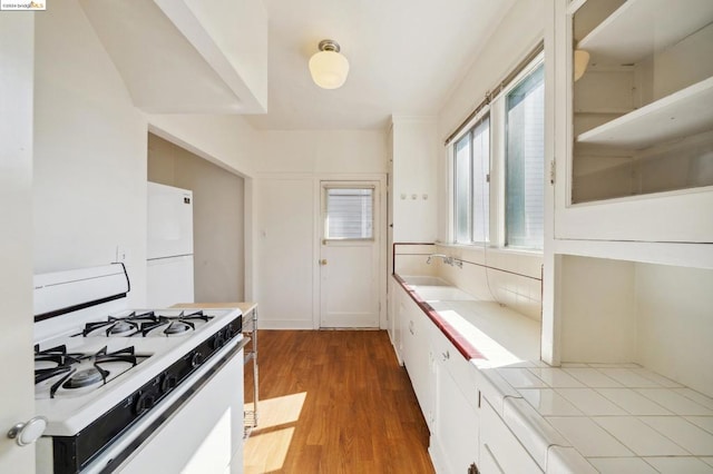 kitchen featuring white appliances, white cabinetry, hardwood / wood-style flooring, and sink