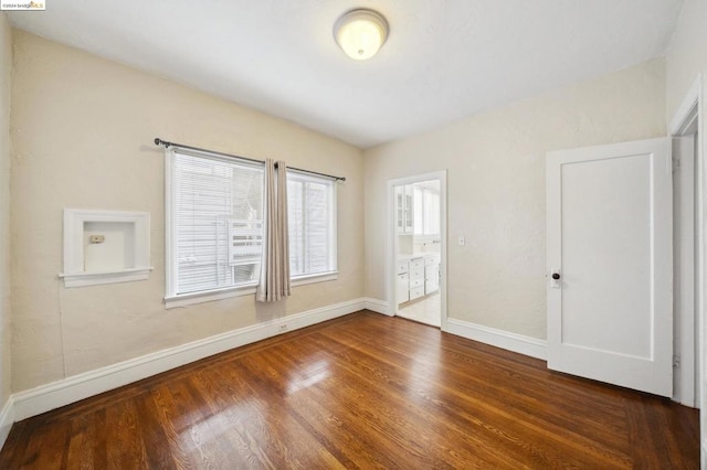 unfurnished bedroom with ensuite bathroom and dark hardwood / wood-style flooring