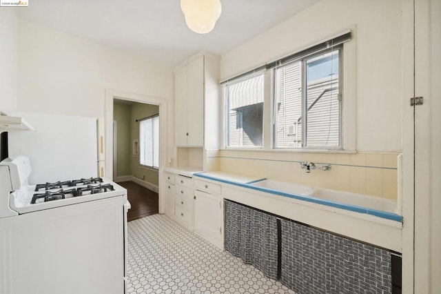 kitchen with ventilation hood, light wood-type flooring, white gas stove, and white cabinets