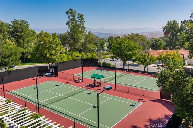 view of tennis court with a mountain view and fence