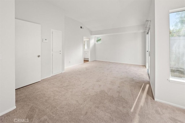 carpeted empty room with vaulted ceiling, a healthy amount of sunlight, visible vents, and baseboards