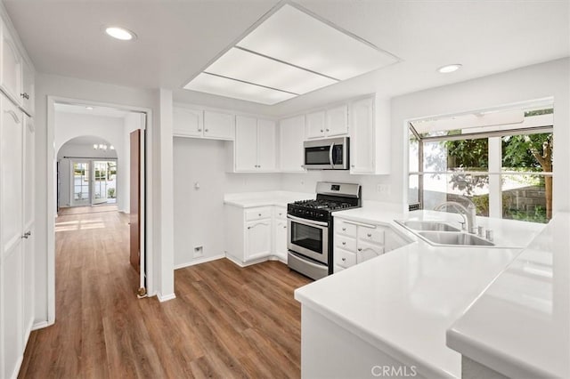 kitchen with white cabinetry, arched walkways, appliances with stainless steel finishes, and a sink