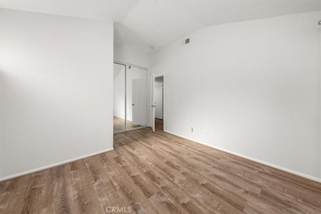 empty room featuring visible vents, baseboards, wood finished floors, and vaulted ceiling