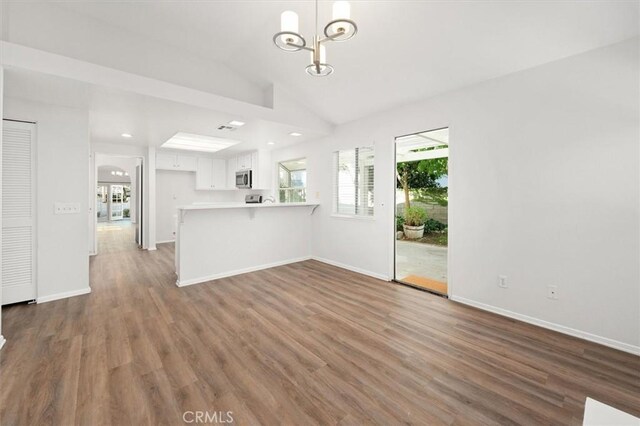 unfurnished living room with lofted ceiling, wood-type flooring, and a notable chandelier