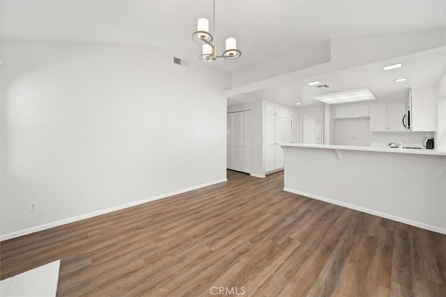 unfurnished living room with dark wood-type flooring, vaulted ceiling, and a notable chandelier