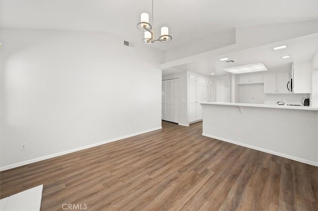 unfurnished living room featuring visible vents, wood finished floors, baseboards, a chandelier, and vaulted ceiling