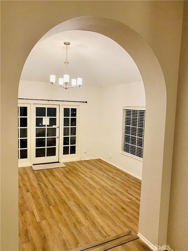 spare room featuring baseboards, an inviting chandelier, and wood finished floors