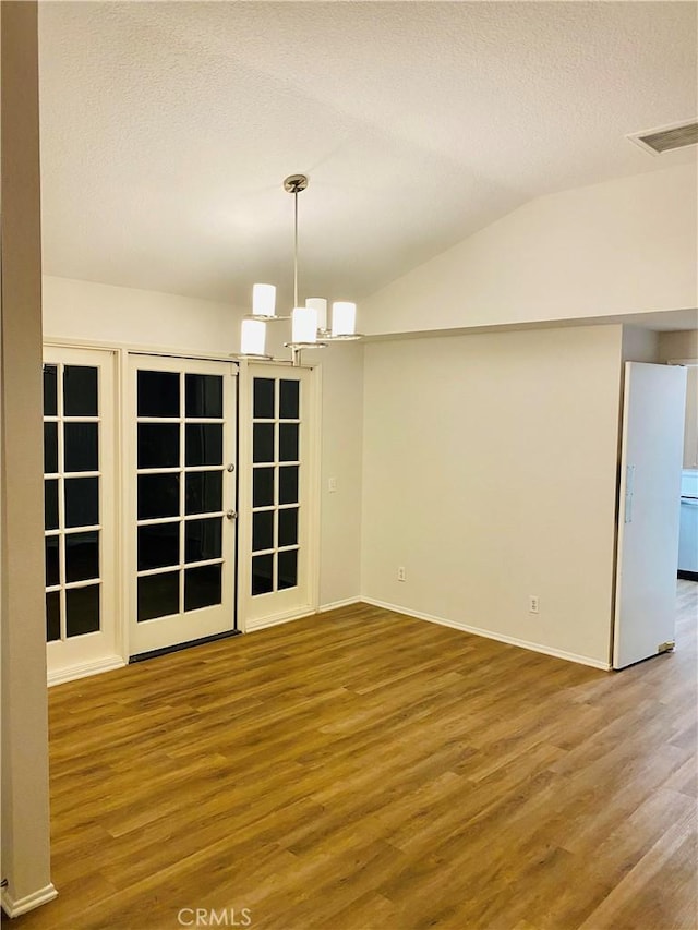 spare room featuring visible vents, vaulted ceiling, an inviting chandelier, wood finished floors, and a textured ceiling