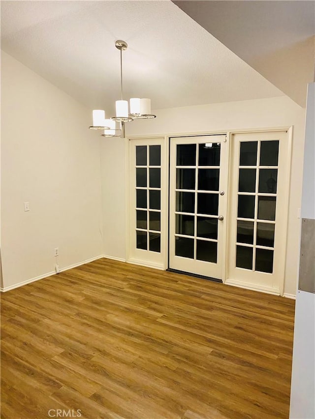 spare room with baseboards, an inviting chandelier, and wood finished floors