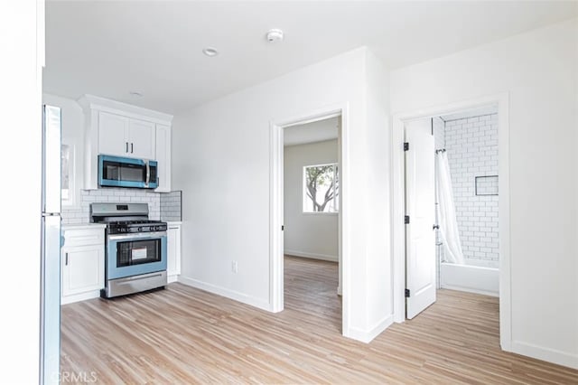 kitchen with white cabinets, light hardwood / wood-style floors, appliances with stainless steel finishes, and tasteful backsplash