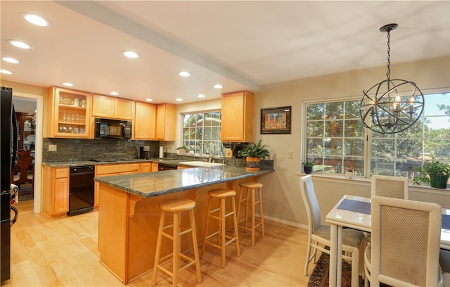 kitchen with hanging light fixtures, dark stone countertops, an inviting chandelier, light hardwood / wood-style floors, and decorative backsplash