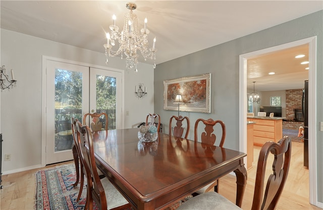 dining area with a brick fireplace, a notable chandelier, french doors, and light hardwood / wood-style floors