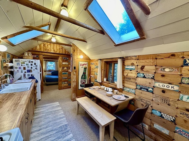 dining space featuring light colored carpet, lofted ceiling with skylight, wooden walls, and sink