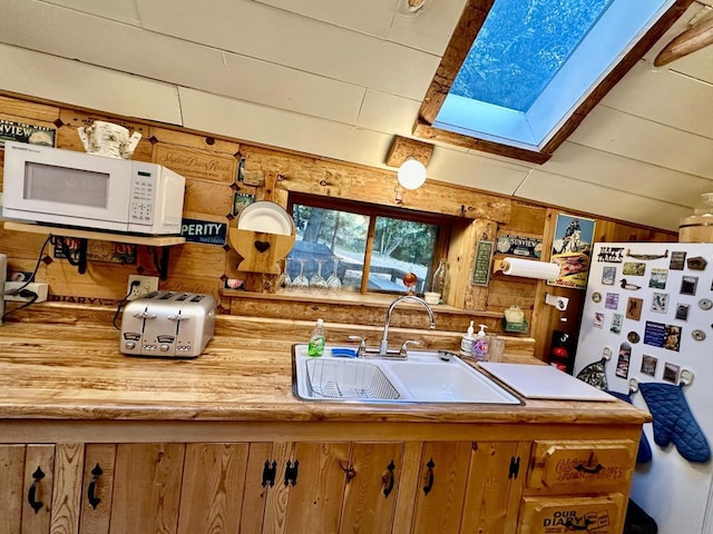 kitchen with sink, lofted ceiling with skylight, fridge, and wooden walls