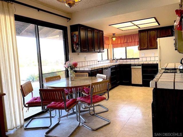 kitchen featuring dark brown cabinets, a textured ceiling, tile countertops, and white fridge