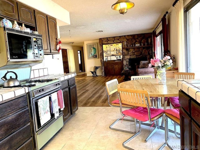 kitchen with gas range oven, dark brown cabinets, a textured ceiling, tile countertops, and light wood-type flooring