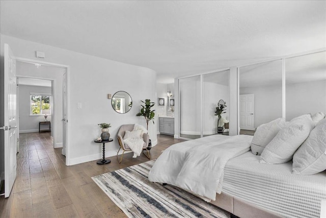 bedroom with connected bathroom, hardwood / wood-style floors, and two closets