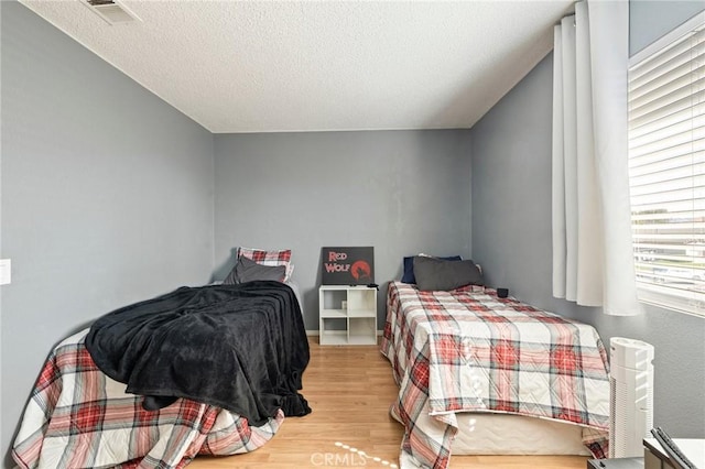 bedroom with a textured ceiling, wood finished floors, and visible vents