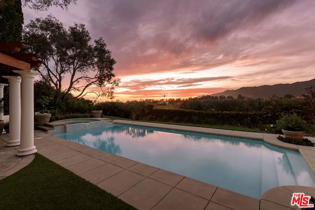 pool at dusk featuring an in ground hot tub and a mountain view