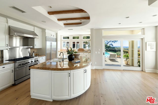 kitchen featuring white cabinetry, premium appliances, wall chimney range hood, and a center island with sink