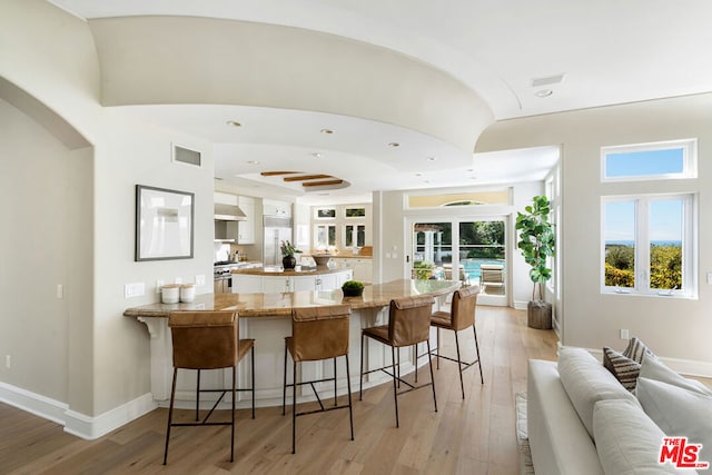 kitchen with a breakfast bar, light hardwood / wood-style floors, kitchen peninsula, wall chimney exhaust hood, and range with two ovens