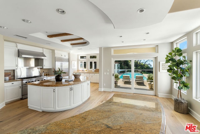 kitchen featuring a kitchen island, high quality appliances, dark stone countertops, white cabinets, and wall chimney exhaust hood