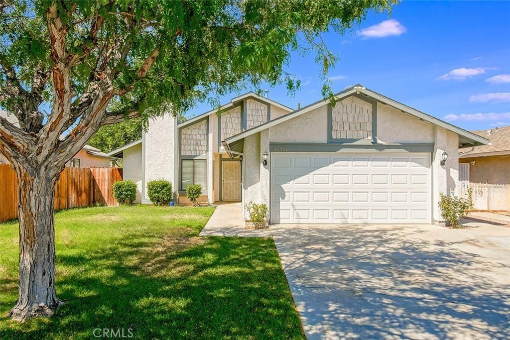 view of front of house featuring a garage, concrete driveway, fence, a front lawn, and stucco siding