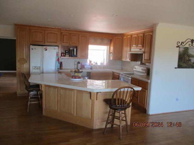 kitchen with tile countertops, a kitchen island, white fridge with ice dispenser, dark hardwood / wood-style flooring, and electric range oven