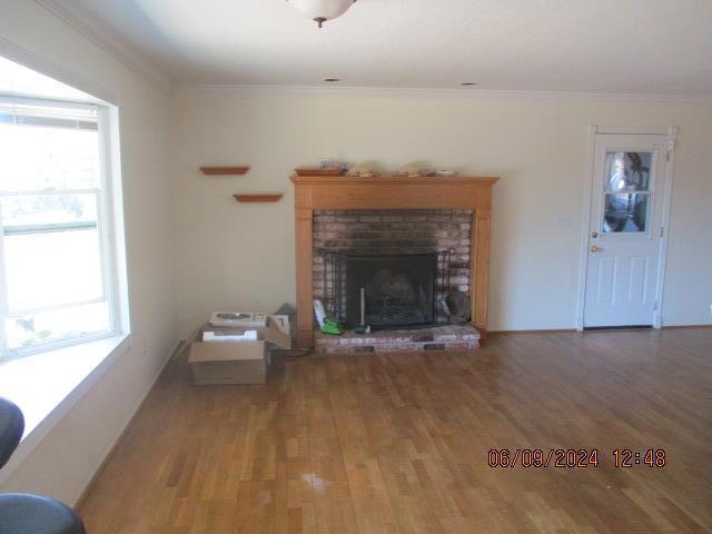 unfurnished living room with a brick fireplace, crown molding, and hardwood / wood-style flooring